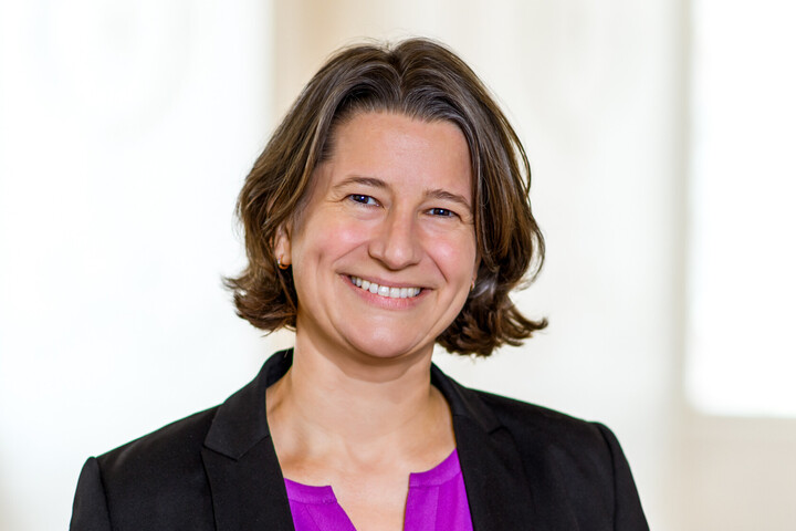 Dr. Katrin Schoppa-Bauer hat braune mittellange Haare. Sie trägt einen schwarzen Blazer und eine lilafarbene Bluse.